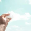 Ręka trzymająca watę cukrową przypominającą chmurę na tle nieba – metafora kreatywnego myślenia i wyobraźni.