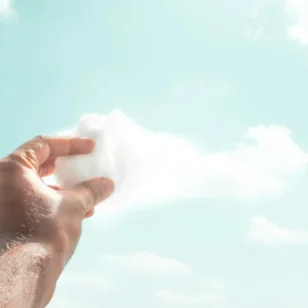 Ręka trzymająca watę cukrową przypominającą chmurę na tle nieba – metafora kreatywnego myślenia i wyobraźni.