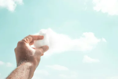 Ręka trzymająca watę cukrową przypominającą chmurę na tle nieba – metafora kreatywnego myślenia i wyobraźni.