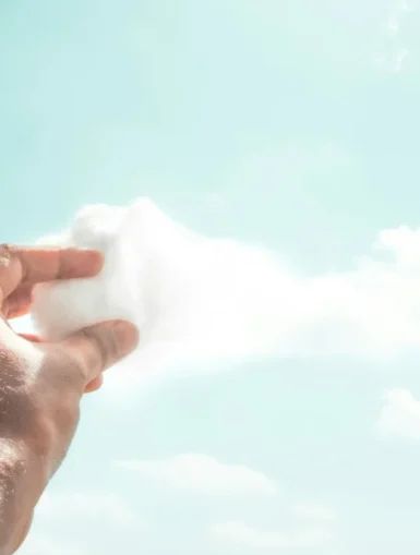 Ręka trzymająca watę cukrową przypominającą chmurę na tle nieba – metafora kreatywnego myślenia i wyobraźni.